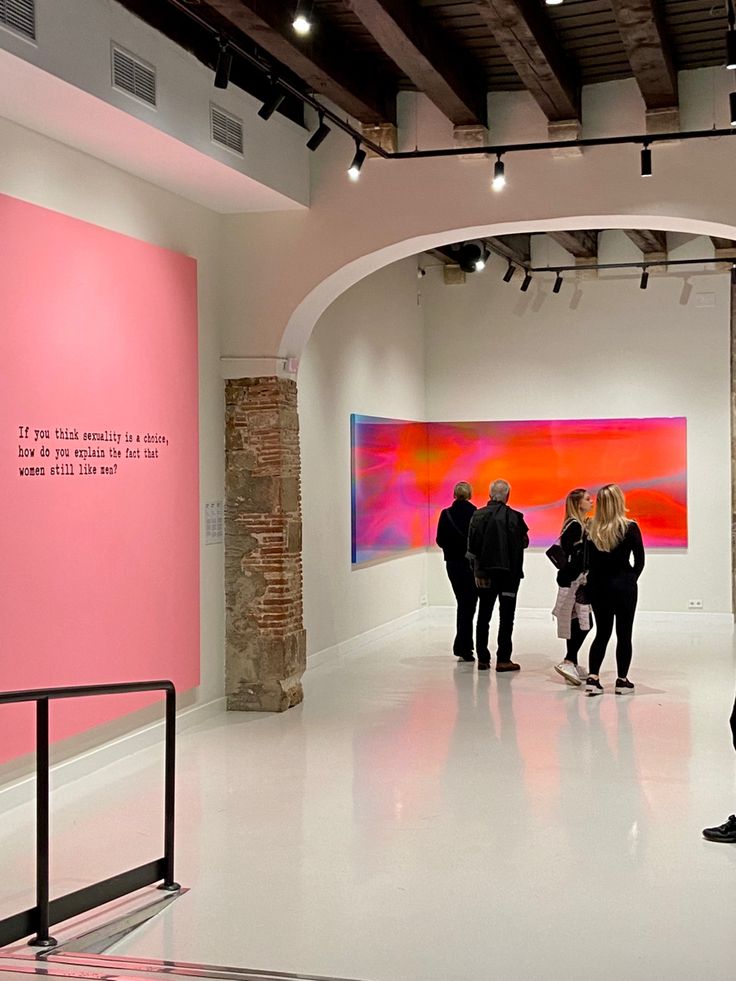 people are looking at art on display in an art gallery with pink and orange paintings