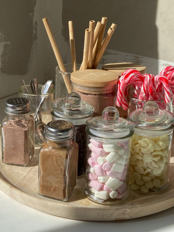 jars filled with candy canes and marshmallows sit on a wooden tray