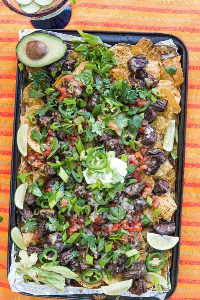 nachos with black beans, avocado and cilantro on an orange striped tablecloth