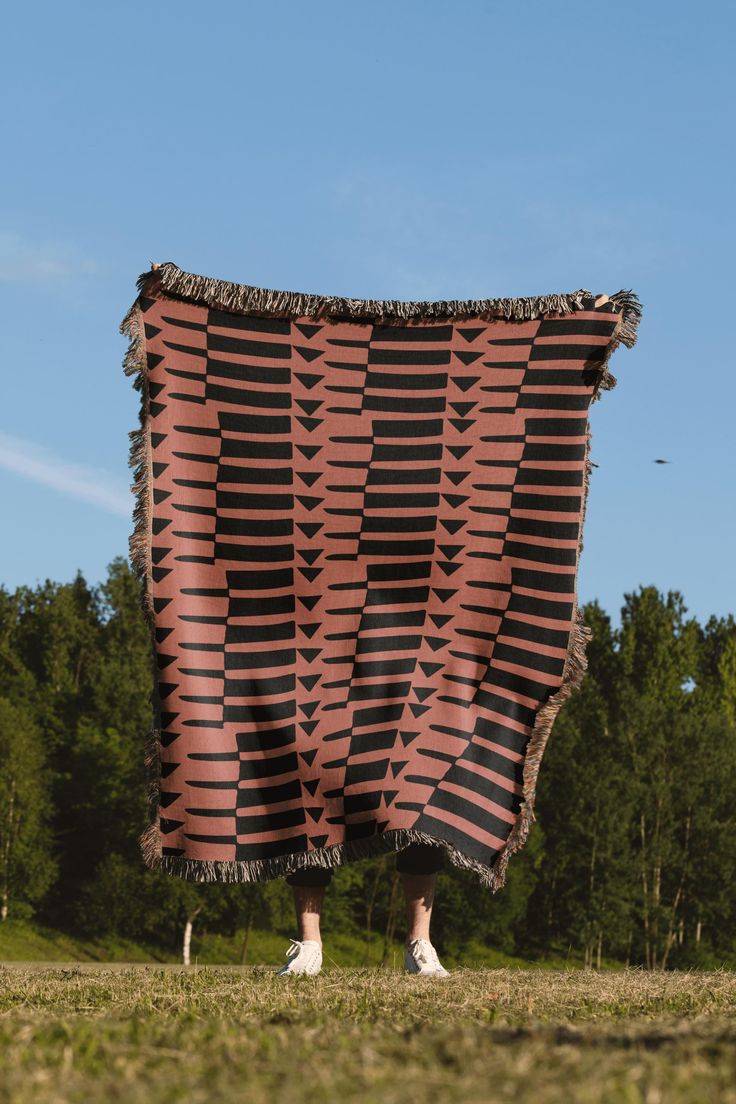 a person standing under a large blanket in the middle of a field with trees behind them