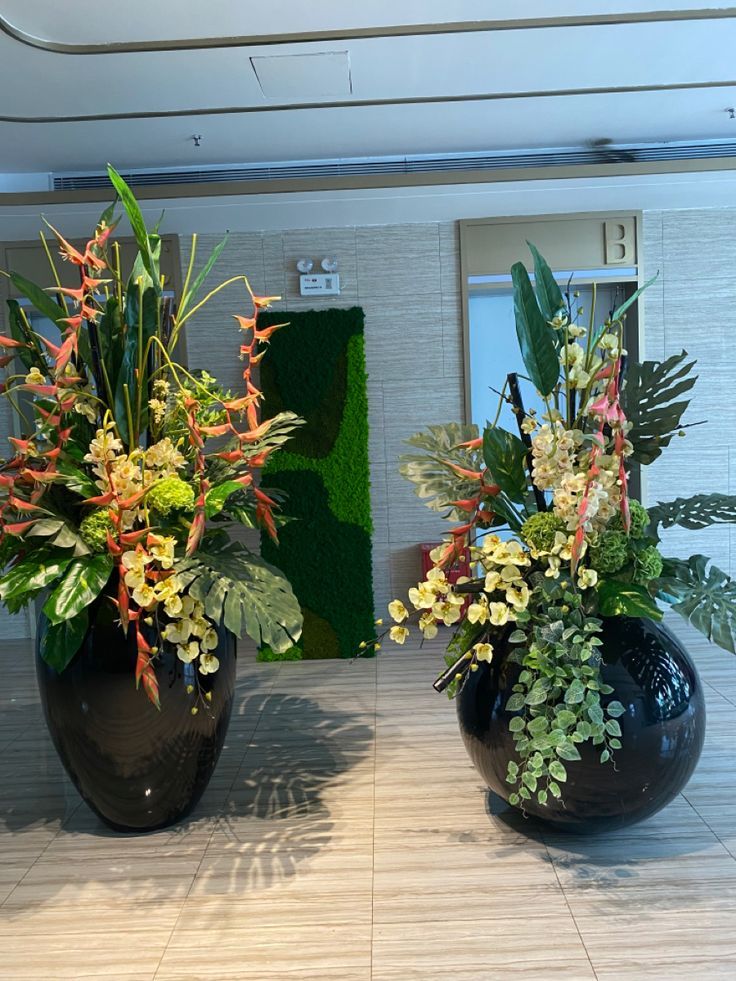 two black vases filled with plants on top of a counter next to each other