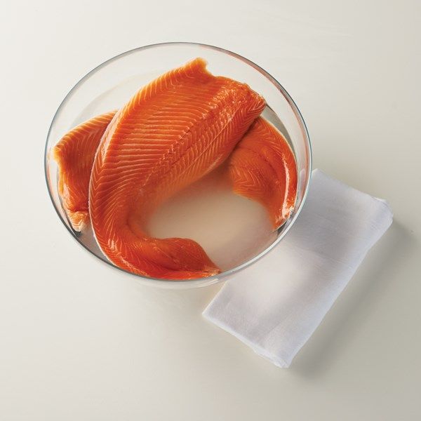 a piece of raw fish in a glass bowl with a napkin on the table next to it