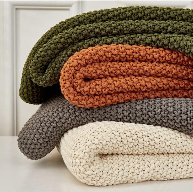 four knitted blankets stacked on top of each other in different colors and sizes, with one folded to the side