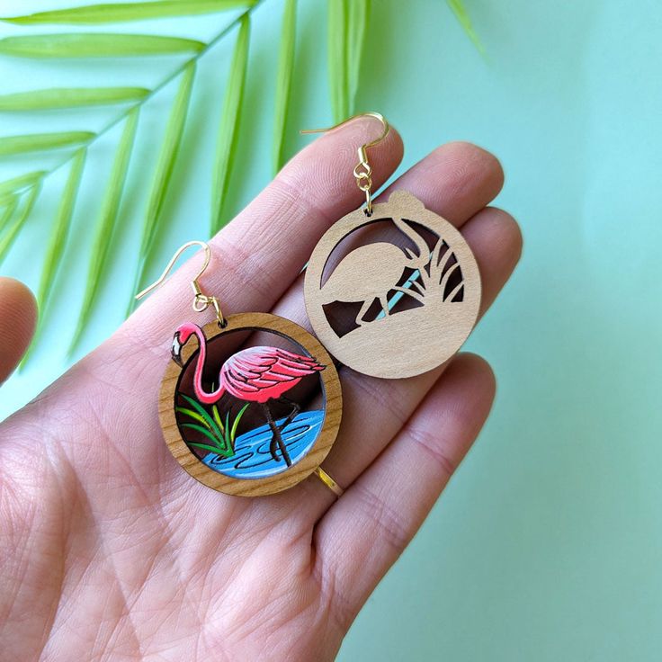 These unique flamingo round dangles are miniature works of art with 2 layers of cherry wood creating a framed vignette of this beautiful bird in its natural habitat. This original design features delicately etched and hand-painted details in a vibrant palette of pink and white, aqua and grass green. The vibrant colors are framed in round cherry wood which creates a a miniature diorama. These earrings are lightweight and durable and make a one-of-a-kind statement for flamingo lovers, birders, gardeners, or anyone who loves nature. Get ready for compliments!Option #1: Painted Wood RoundsThese earrings feature painted cherry wood rounds with hypoallergenic gold-finished, 304 stainless steel studs and butterfly backs. Drop Length: 2"Option #2: Gold Ear WiresThese earrings feature hypoallergeni Miniature Diorama, Wood Studs, Beautiful Bird, Grass Green, Wood Rounds, Pink Flamingo, Gift Card Shop, Pink Flamingos, Painted Wood