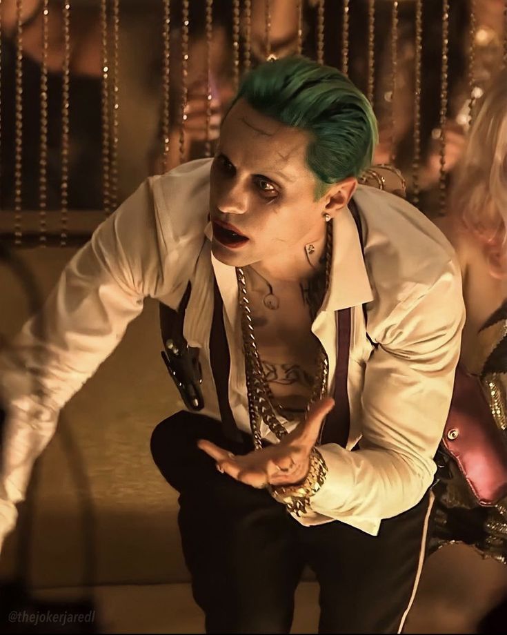 a man with green hair and piercings crouching down in front of a mirror