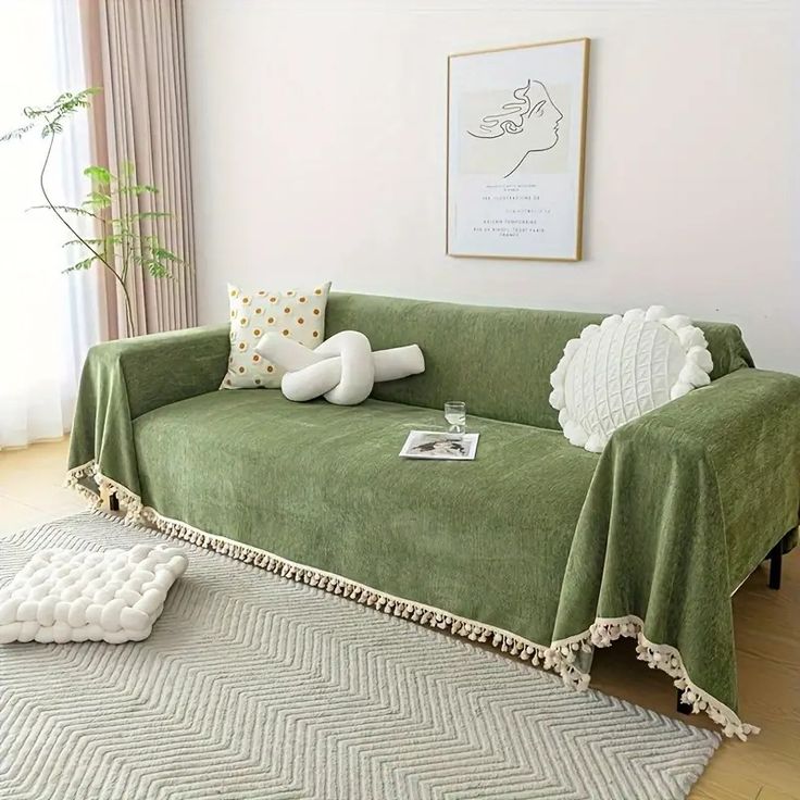 a living room with a couch covered in a green cover and pillows on the floor