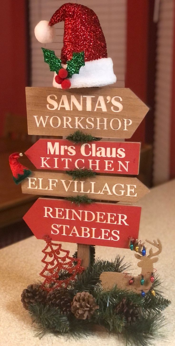 a wooden sign with santa's workshop, mrs claus and elf hats on it