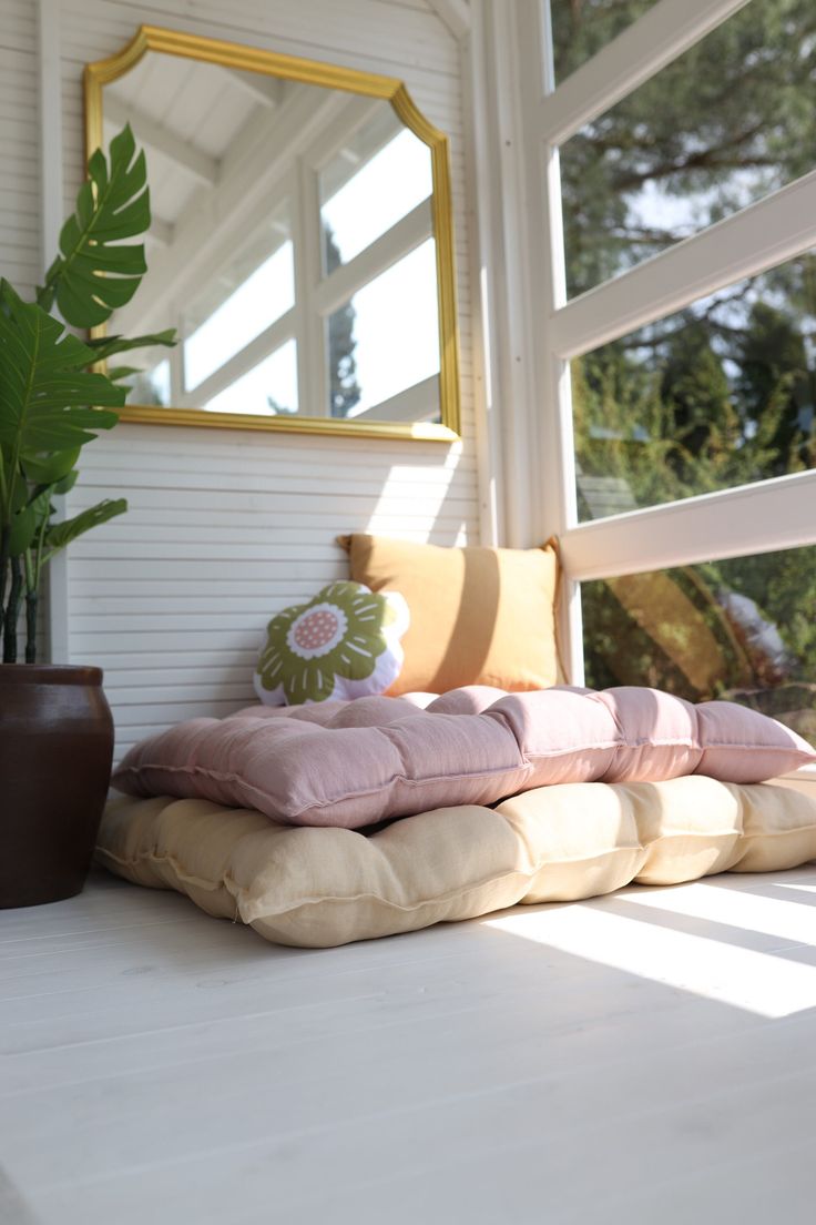 pillows are stacked on top of each other in front of a large mirror and potted plant