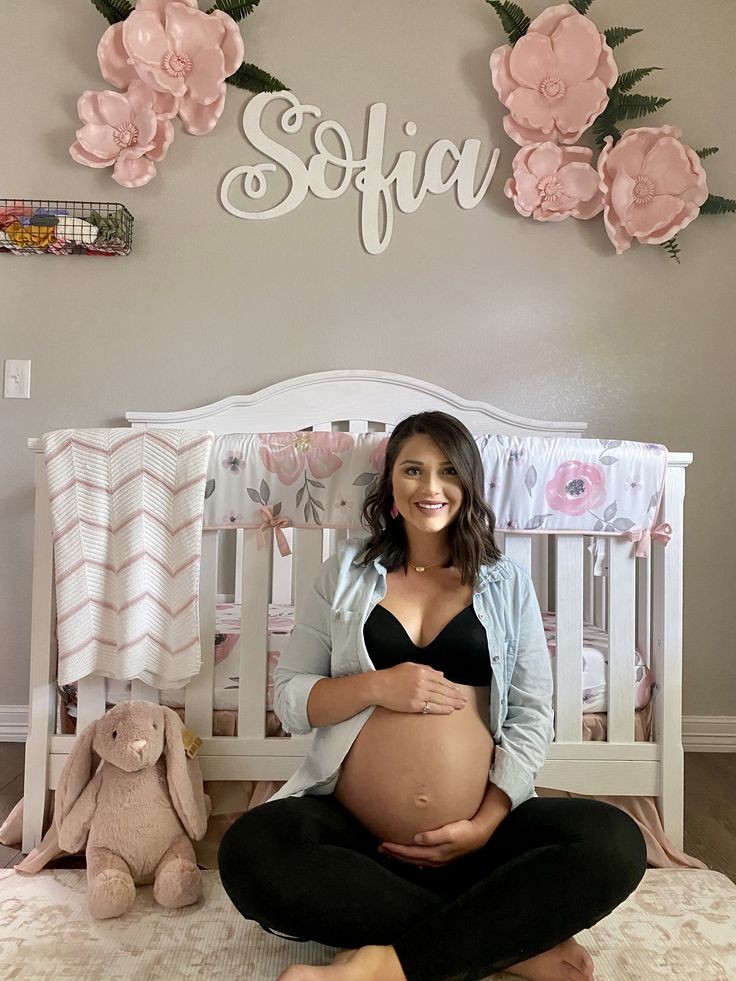 a pregnant woman is sitting on her bed in front of the wall with pink flowers