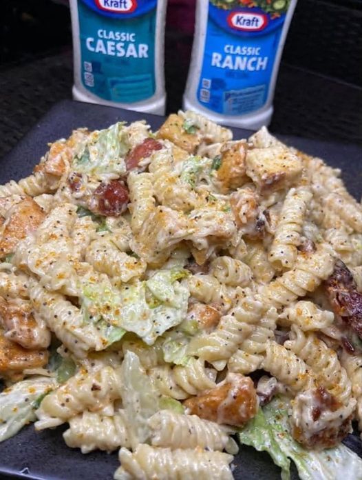 the pasta salad is ready to be eaten on the table next to two bottles of ranch dressing