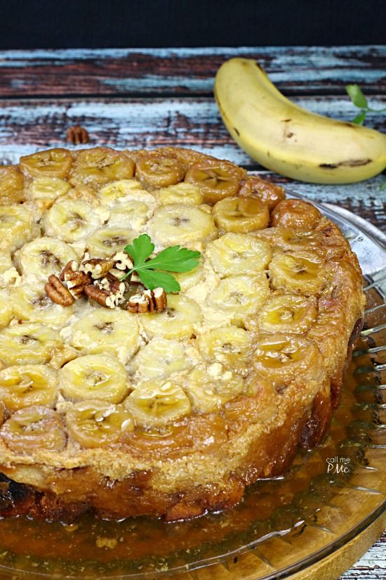 a cake on a glass plate with bananas and pecans around it, sitting on a wooden table