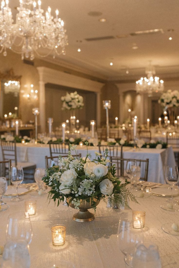 the centerpieces on this table are white roses and greenery with candles in them