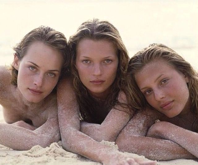 three women laying in the sand with their arms around each other and looking at the camera