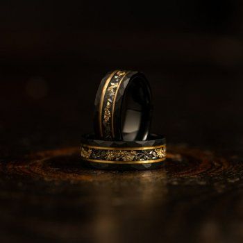 two black and gold wedding bands on top of each other in front of a dark background