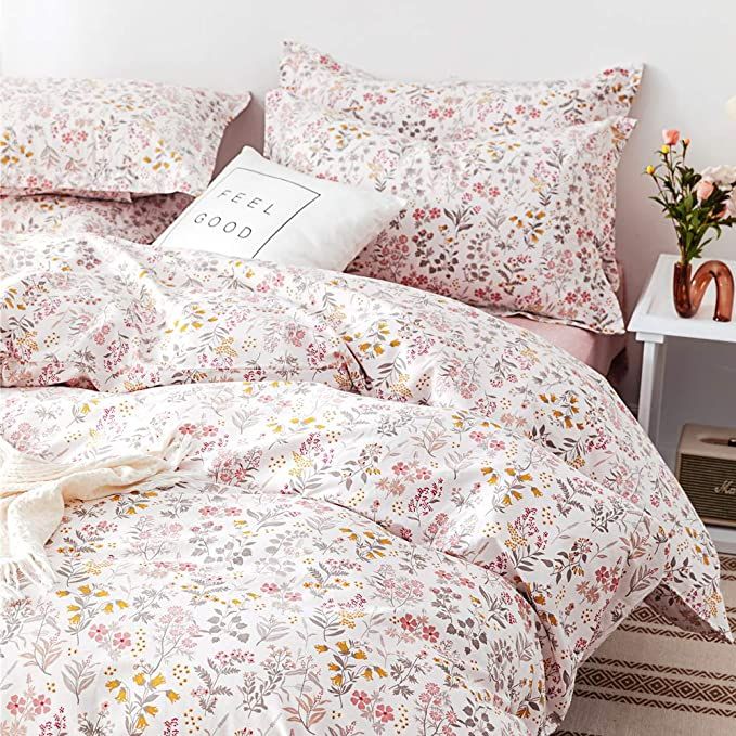 a bed covered in pink and yellow floral comforter with pillows on top of it