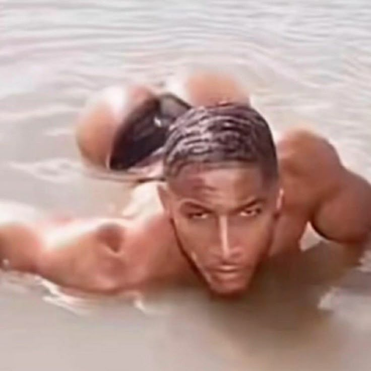 a shirtless man is in the water with his head above his chest and hands behind his back