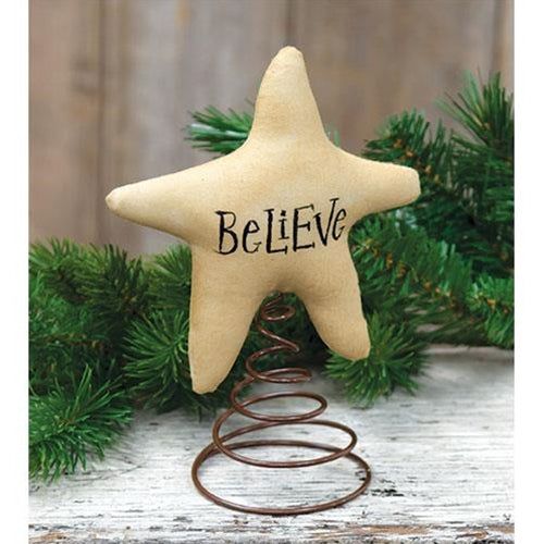 a star ornament with the word believe on it sitting next to a pine tree