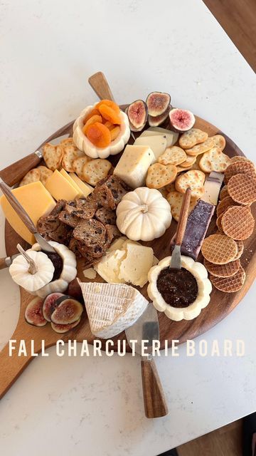 a wooden platter filled with different types of cheese and crackers on top of a white table