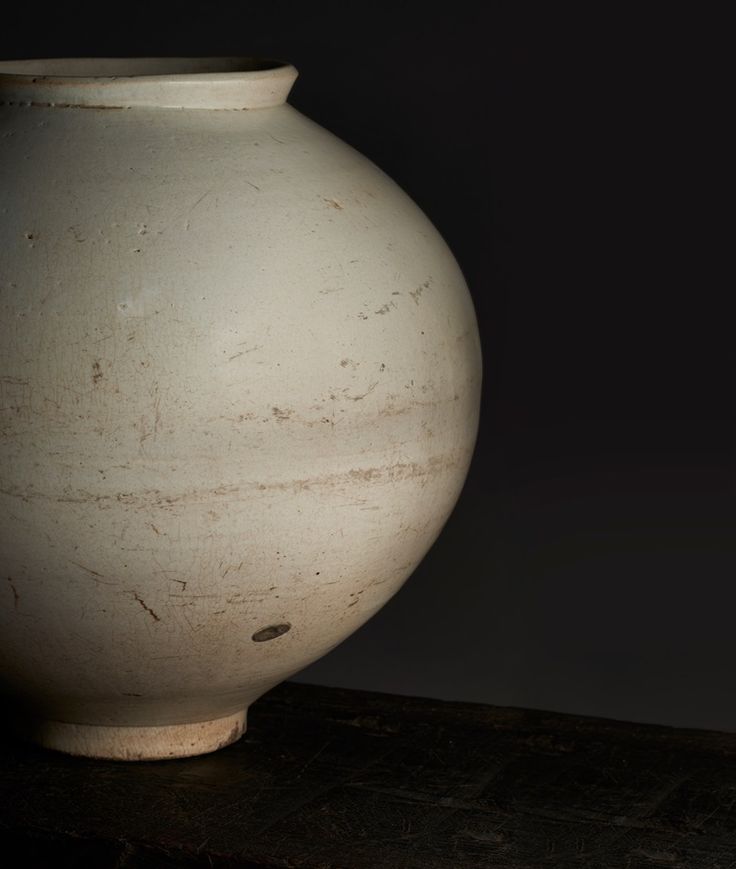 a large white vase sitting on top of a wooden table next to a black wall