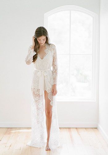 a woman standing in front of a window wearing a white lace robe and high heels