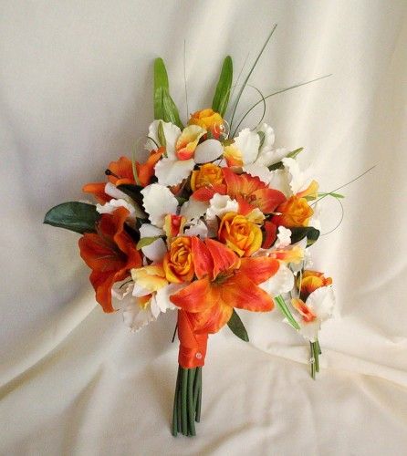 a bridal bouquet with orange and white flowers on a white cloth draped in the background