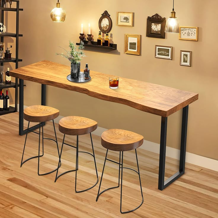 a dining table with stools in front of it and pictures on the wall behind it