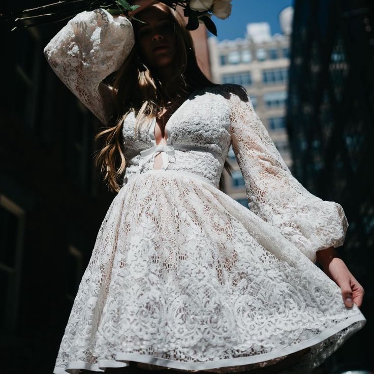 a woman wearing a white dress and holding flowers on her head in the middle of a city