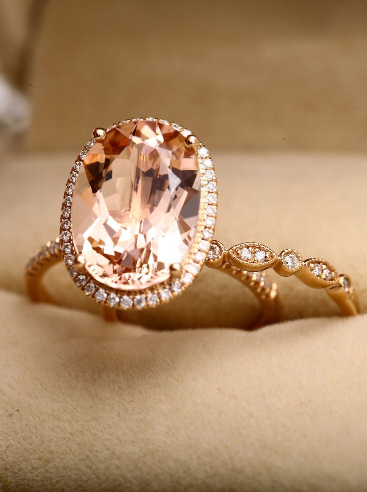 an oval shaped morganite and diamond ring in gold with diamonds around the band on a cushioned surface