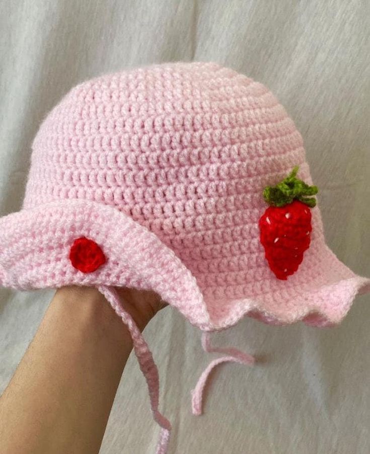 a crocheted pink hat with two strawberries on the brim is held up