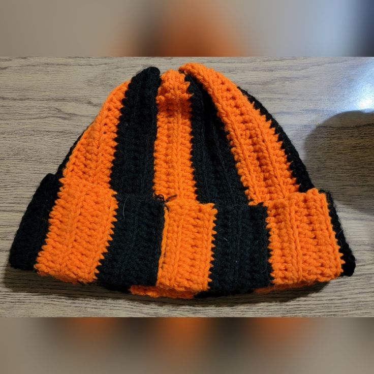 an orange and black knitted hat sitting on top of a wooden table