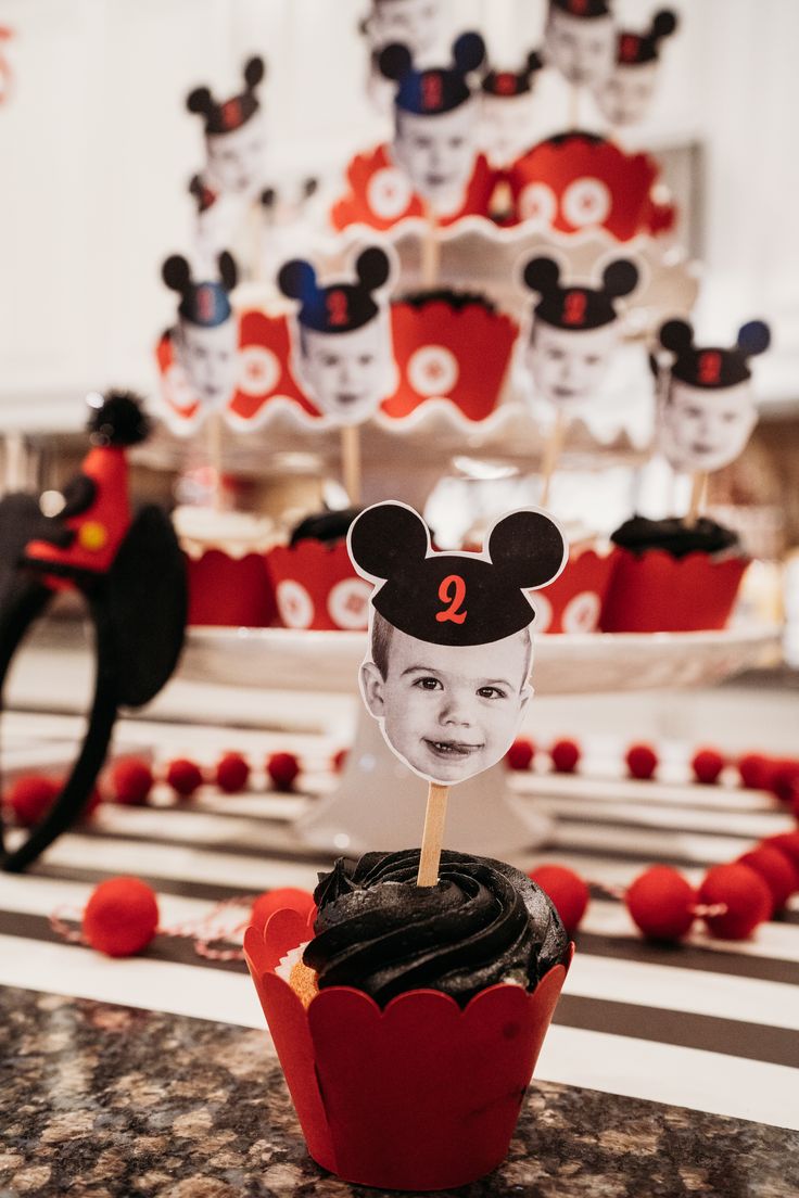 a cupcake with a mickey mouse topper on it sitting in front of a cake