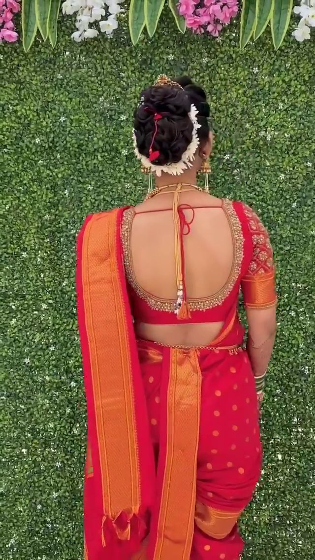 a woman in red and orange sari standing on the grass with flowers behind her