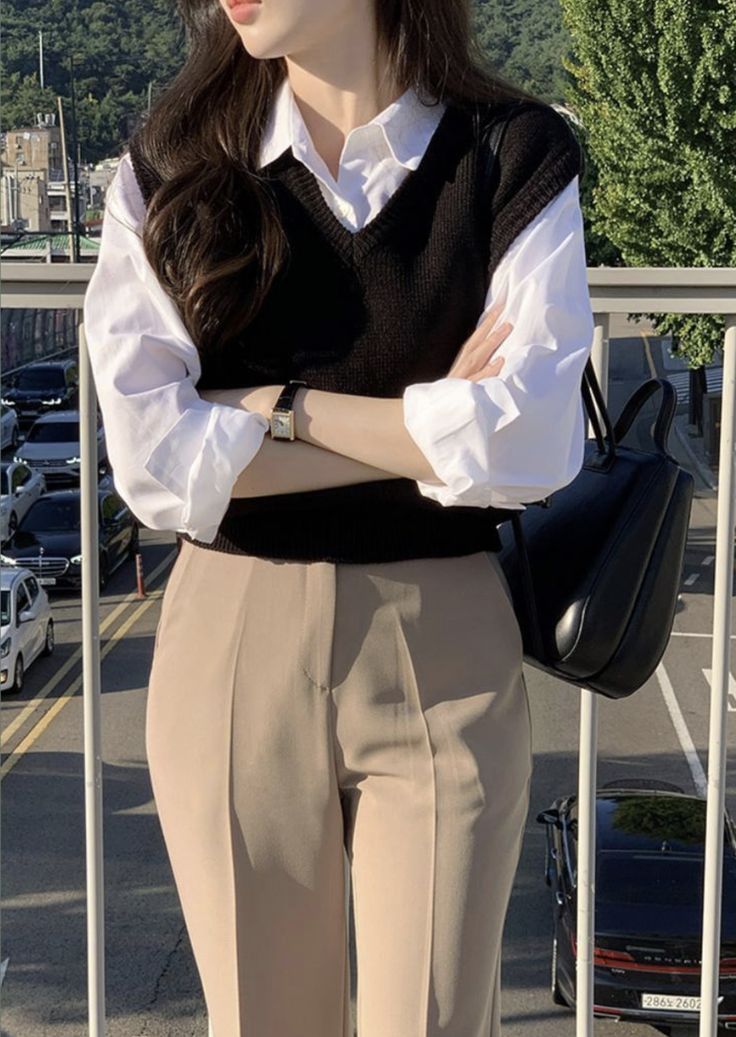 Achieve a timeless and polished look with this classic layered outfit featuring a black knit sweater vest over a crisp white button-down blouse. Paired with tailored beige trousers, casual and sophisticated. Whether for work or a coffee date, this look delivers effortless elegance. Accessorized with a sleek black leather bag and minimalist watch.  #LayeredLook #ClassicOutfit #BusinessCasual #MinimalistFashion #EffortlessChic #OOTD #styleguide Sweater Vest Formal Outfit, T Shirt With Jeans Outfits, Korean Classy Outfits, Aesthetic Lawyer, Neat Casual Outfits, Simple Casual Outfits, Lawyer Fashion, Casual Work Outfits Women, Casual College Outfits