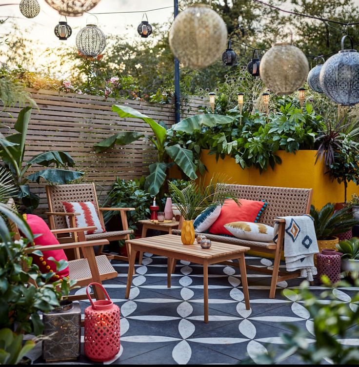 an outdoor seating area with potted plants and hanging lights in the background, surrounded by greenery