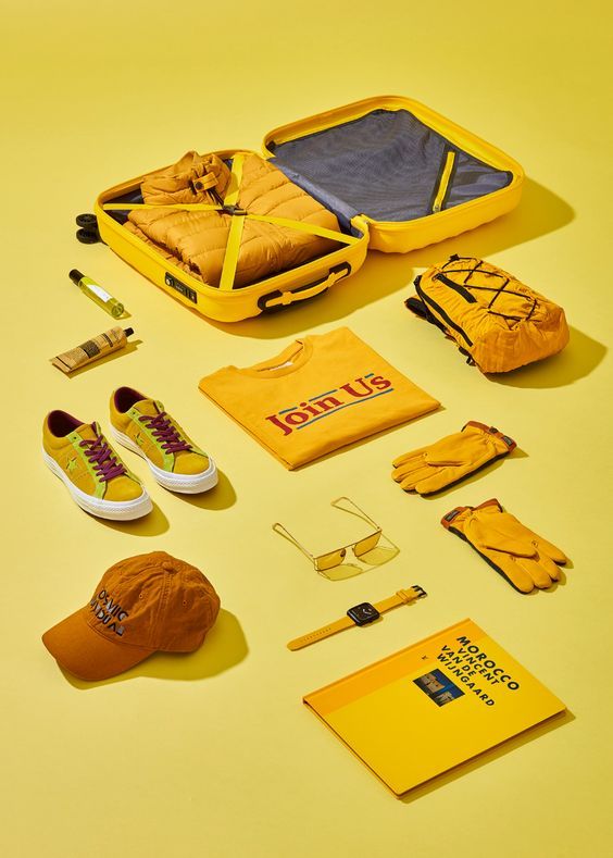 an assortment of clothing and accessories laid out on a yellow surface, including shoes, backpacks, hat, t - shirt, sunglasses