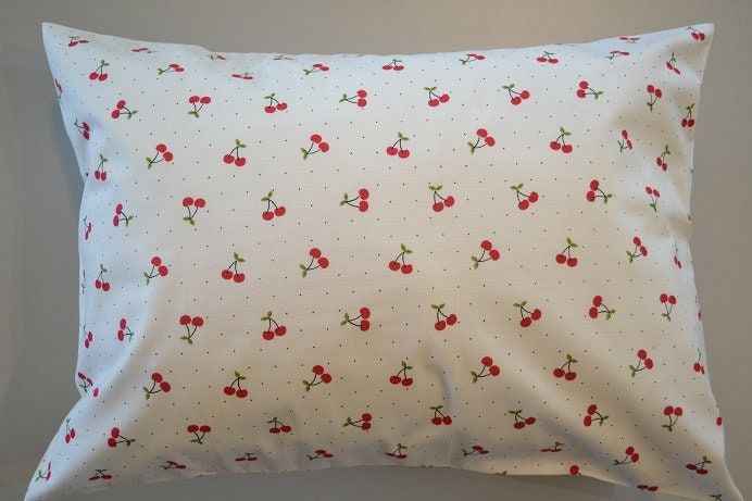 a white pillow with red cherries and polka dots on it's back side