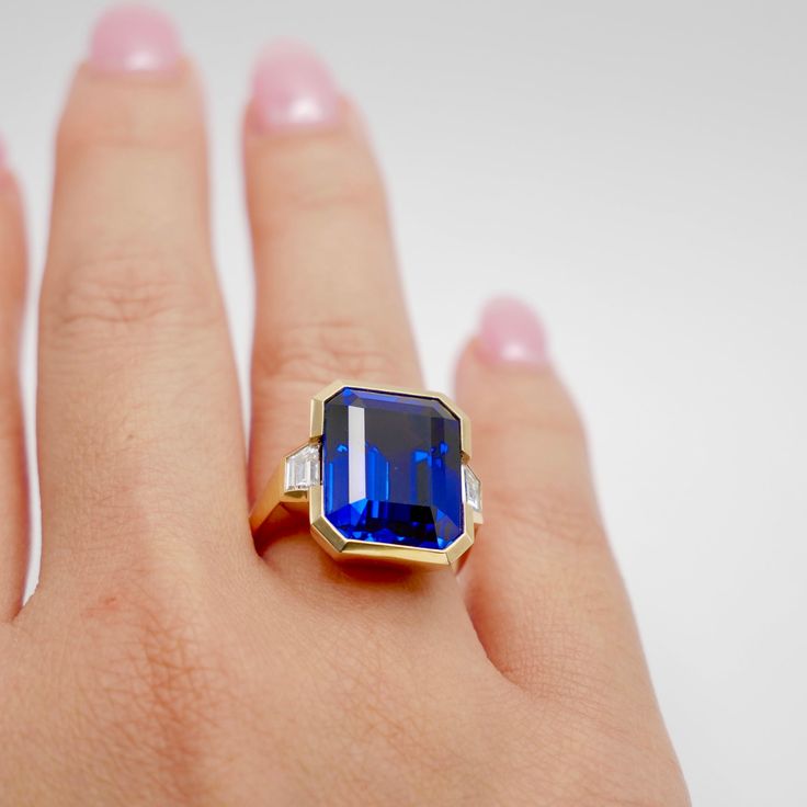 This exquisite 12 Ct Lab Grown Emerald Cut Sapphire and Trapezoid Diamond Ring is masterfully set in 18K yellow gold. This piece captures the essence of modern elegance with its sharp, clean lines and a striking bezel setting. Flanked by trapezoid diamonds, the sapphire centerpiece exudes a royal blue hue. Perfect for those who cherish contemporary design with a hint of classic allure. Luxury Octagon Brilliant Cut Sapphire Ring, Luxury Octagon Sapphire Ring With Brilliant Cut, Luxury Gia Certified Baguette Cut Sapphire Ring, Gia Certified Octagon Sapphire Ring, Luxury Style, Gia Certified Octagon Sapphire Luxury Ring, Luxury Gia Certified Octagon Sapphire Ring, Luxury Yellow Gold Gia-certified Sapphire Ring, Luxury Gia Certified Yellow Gold Sapphire Ring, Luxury Emerald-cut Sapphire Ring With 17 Jewels