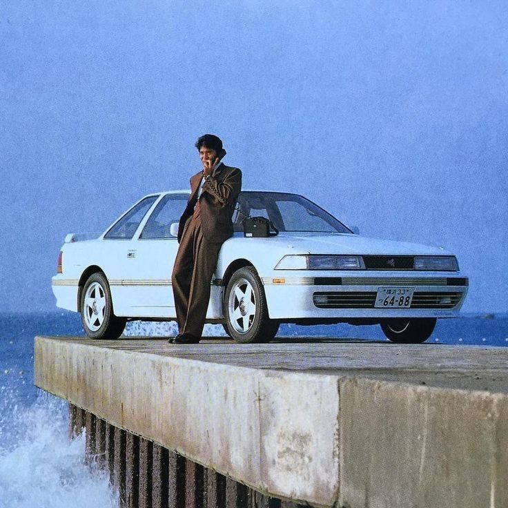 a man standing next to a white car on top of a pier near the ocean