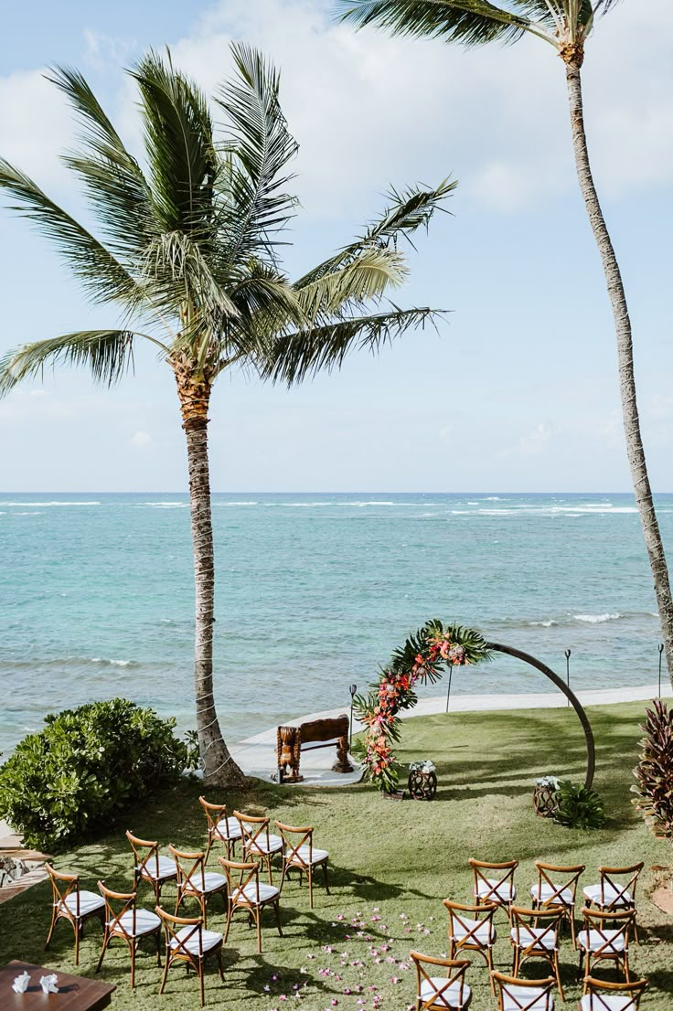 chairs set up for an outdoor ceremony on the beach with palm trees in the foreground