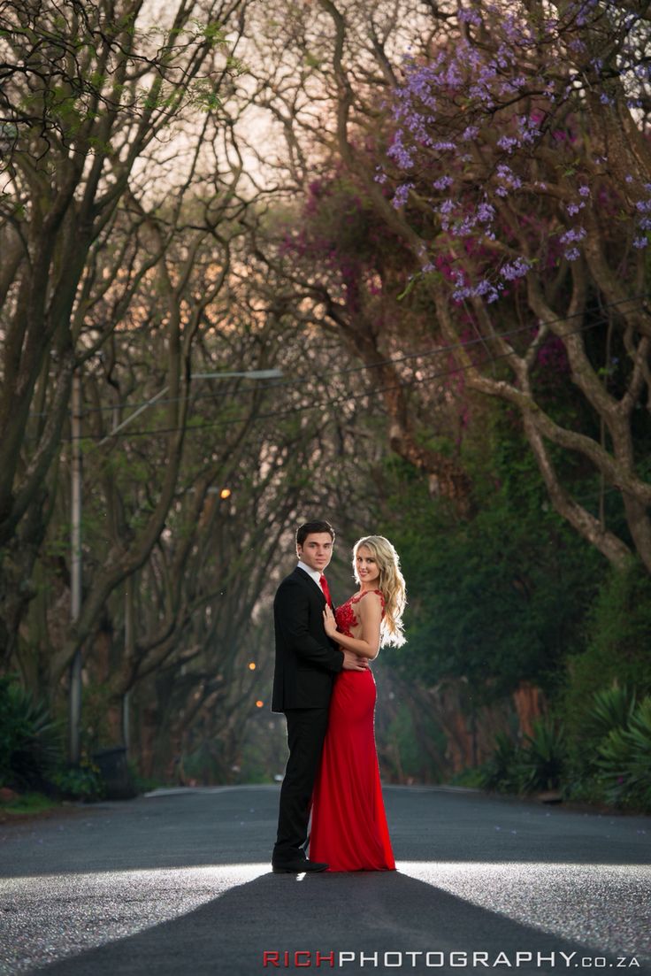 a man and woman standing in the middle of an empty road with trees behind them