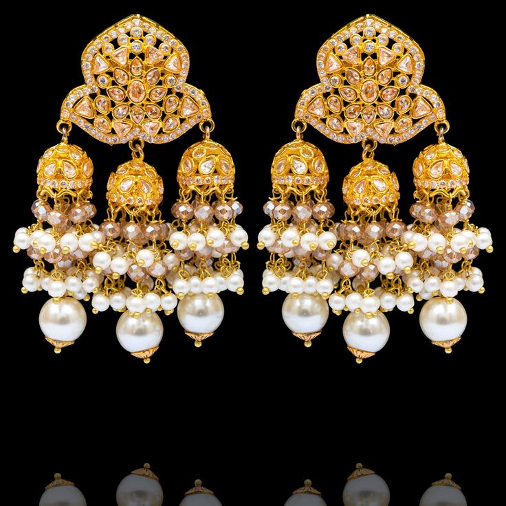 Elevate your look with the perfect blend of modern flair and timeless charm! Unveil your next go-to accessory with grace as these statement earrings feature a dazzling array of CZ stones in a beautifully intricate design, culminating in a triple jhumki style complemented with a cascade of lustrous pearls that adds a touch of opulence to your every movement. Approximate earrings length is 2.75". Gold-plated on high-quality brass as base metal. Made by order. Kindly allow 5-7 weeks for the deliver White Danglers With Intricate Design For Reception, Festive Bridal Chandbali Earrings With Elegant Design, Diwali Reception Chandelier Earrings With Stone Work, Bollywood Earrings With Intricate Design For Reception, Gold Chandelier Earrings With Stone Work, Bollywood Style Chandelier Earrings With Intricate Design For Reception, Gold Fusion Chandelier Earrings With Stone Work, Bollywood Style Earrings With Intricate Design For Reception, Stone Work Drop Earrings For Reception