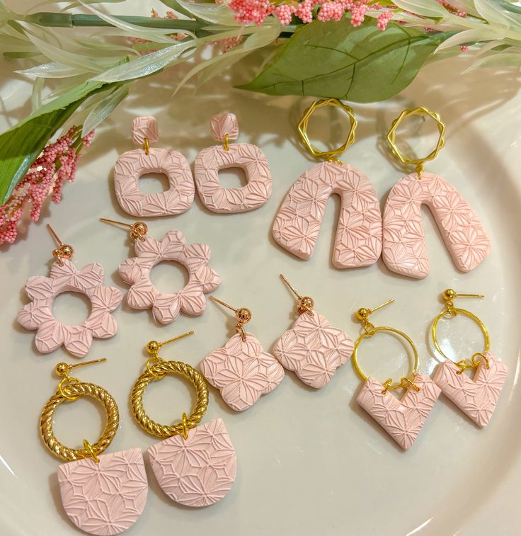 pink and gold earrings on a plate next to flowers