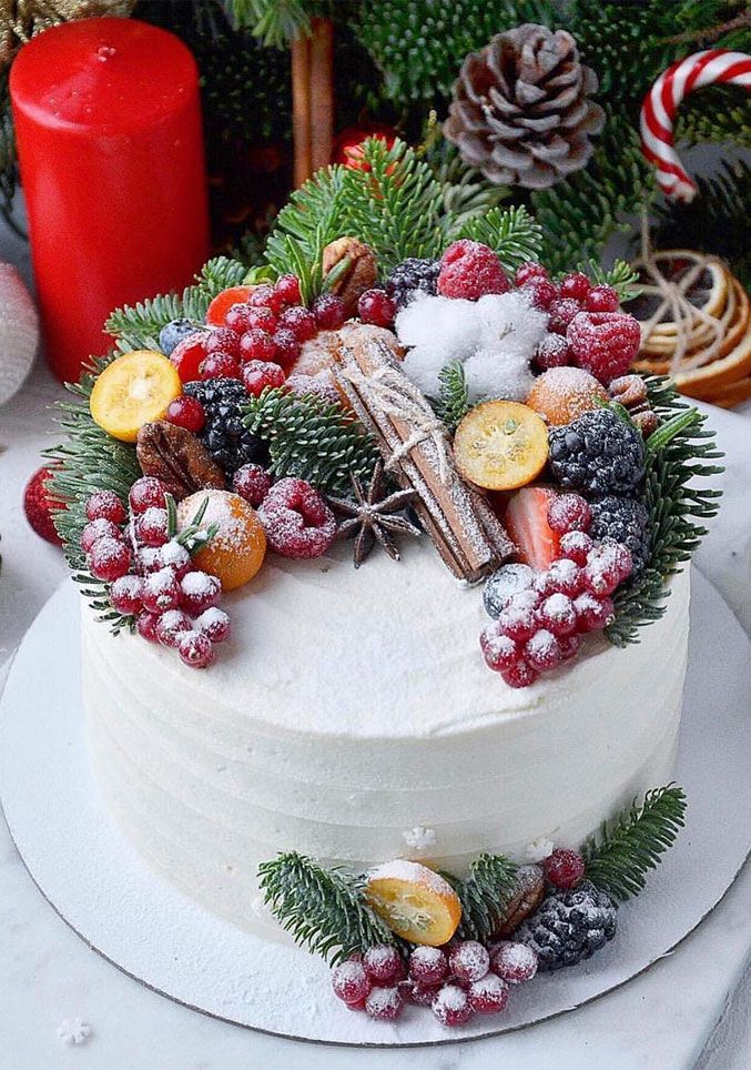 a white cake decorated with berries, pine cones and cranberries on a table