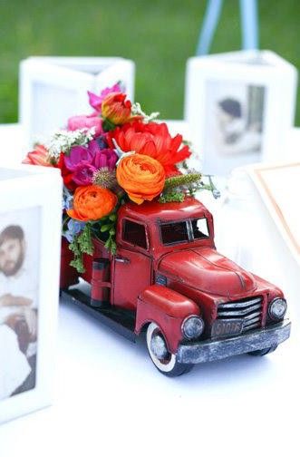 an old red truck with flowers in it is sitting on a table next to pictures