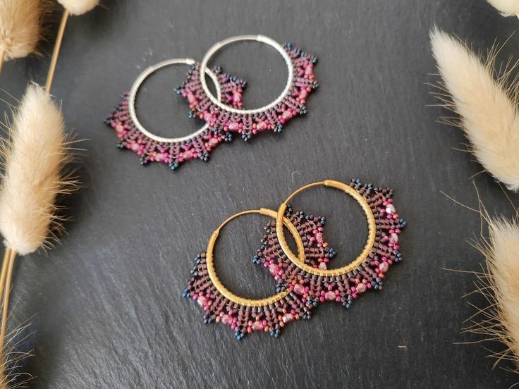 three pairs of beaded hoop earrings sitting on top of a black surface next to feathers