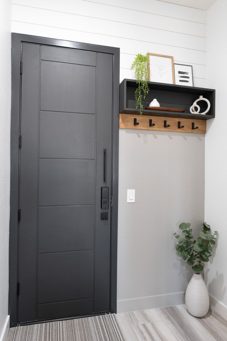 an entryway with a black door and shelf on the wall, next to a potted plant