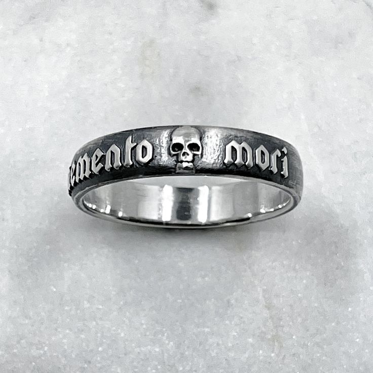 The Memento Mori Ring is not just a piece of jewellery; it is a talisman of empowerment and introspection. By wearing this ring, you carry a symbol of your own mortality, inviting reflection and inspiring a deeper appreciation for the fleeting beauty of life. It serves as a reminder to live fully, embracing the joys and challenges that come your way. Memento mori is a Latin phrase meaning 'remember you must die' Ring is 6mm wide. 925 Sterling Silver. Each piece is handmade to order in our Jewel Spiritual Promise Rings With Engraving Option, Symbolic Etched Jewelry For Promise, Symbolic Handmade Engraved Promise Ring, Handmade Symbolic Engraved Ring For Promise, Symbolic Engraved Skull Ring Gift, Symbolic Engraved Skull Ring For Gift, Symbolic Skull Ring For Anniversary, Symbolic White Gold Skull Ring For Anniversary, Symbolic Engraved Ring With Oxidized Finish For Promises