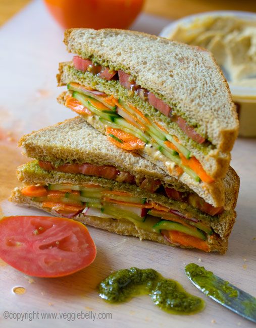 a cut in half sandwich sitting on top of a cutting board next to a slice of tomato