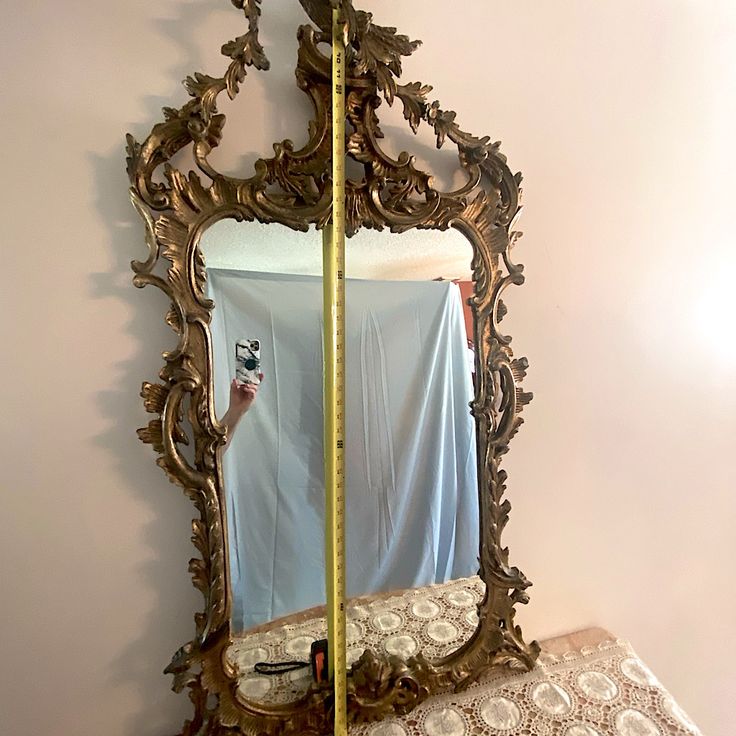 an ornate gold mirror is hanging on the wall next to a bed with a sheet draped over it