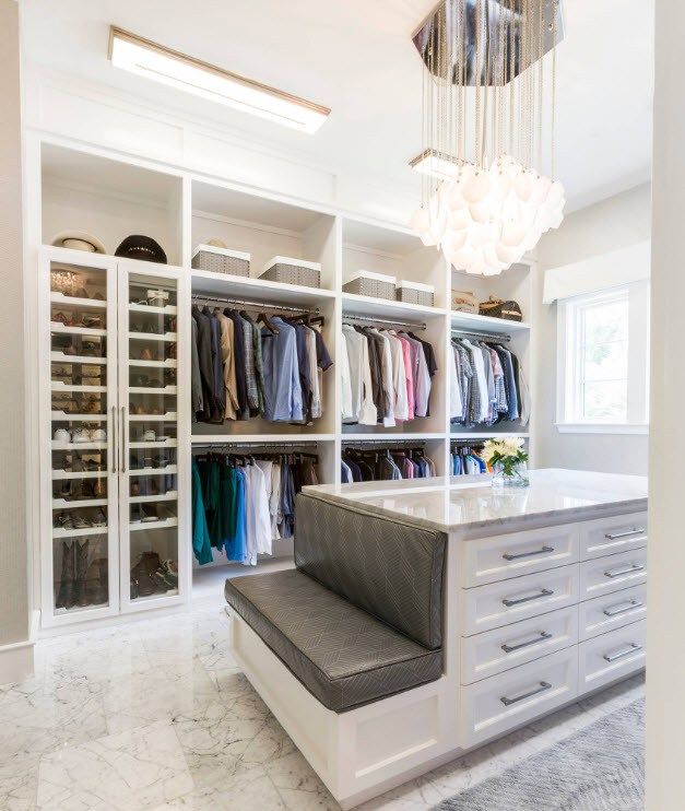 a walk in closet with lots of clothes on shelves and a bench next to it